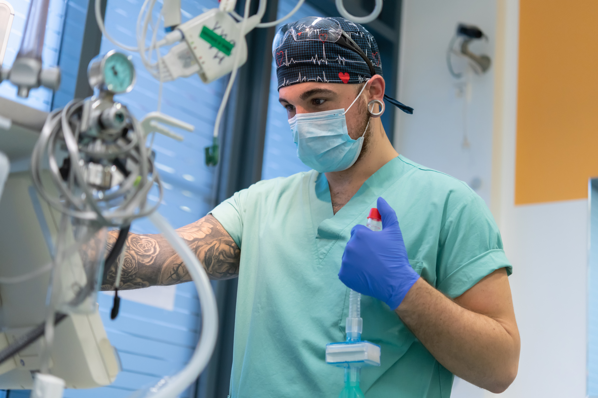 Ein junger Mann im Klinik-Kittel und mit OP-Maske überwacht einen medizinischen Monitor.