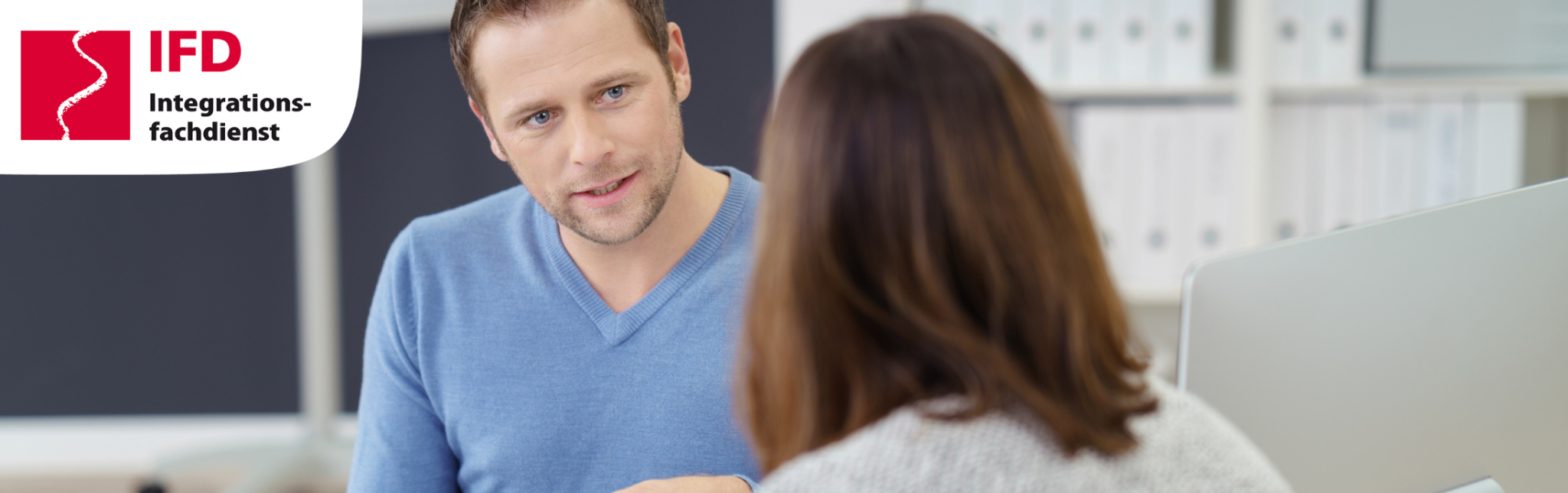 Ein Mann mit blauem Pulli befindet sich in einer Beratungssituation mit einer Frau, die man nur von hinten sieht. Ein Logo zeigt, dass es sich um den Integrationsfachdienst handelt. 