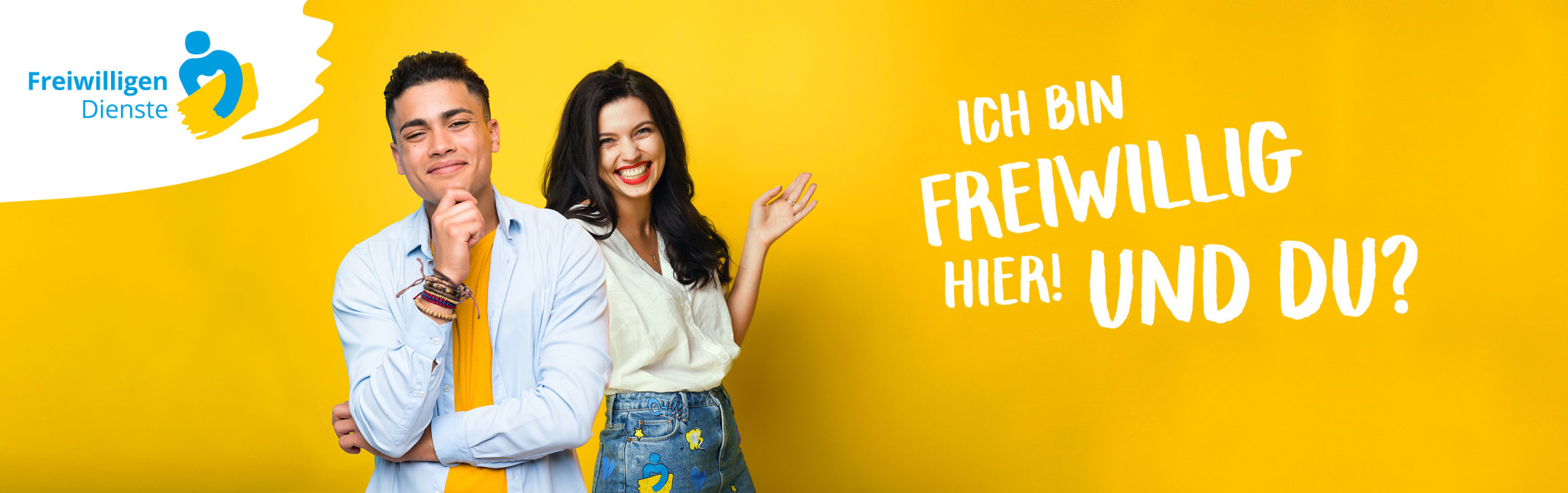 Junger Mann und junge Frau vor gelbem Hintergrund mit der Aufschrift "Ich bin freiwillig hier! Und du?". Links oben befindet sich auf einem weißen Hintergrund das IB Freiwilligendienste Logo: blaues Strichmännchen mit herzförmig geschwungenen Armen hält gelben Pinselstrich, daneben Text: Freiwilligen Dienste.