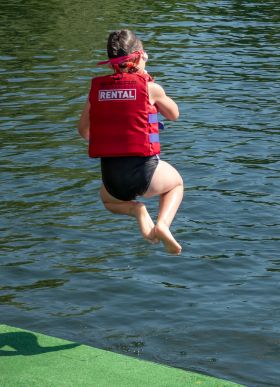 Mädchen springt im Schwimmanzug und Schwimmweste ins kühle Nass