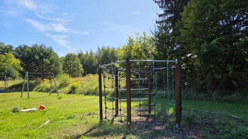 Ein Garten mit einer Zip-Line und einem Klettergerüst, umgeben von Bäumen.