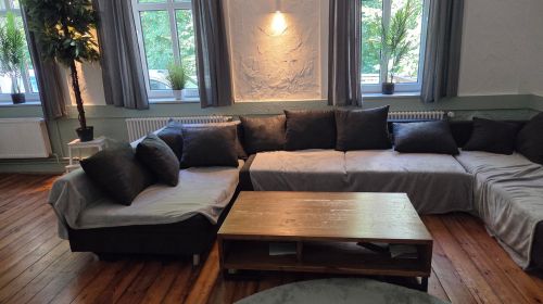 Ein Wohnzimmer mit einem Wohnzimmer, Wohnzimmertische und drei großen Fenstern mit Pflanzen auf den Fensterbänken.