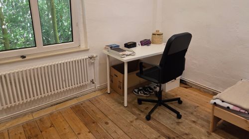Ein Zimmer mit Heizkörper, Fenster, Schreibtisch und Schreibtischstuhl.