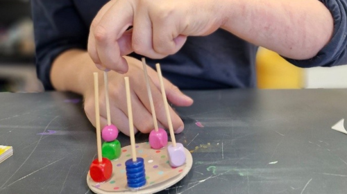 Man sieht Hände und ein Holzspiel, vermutlich Kreisel. 