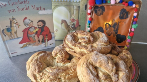Man sieht einen Teller voller Martinsbrezeln. Dahinter steht ein Buch zum Thema "St. Martin".