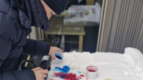 Eine Person mit Winterjacke und Mütze bemalt etwas. Sie ist kreativ tätig. 