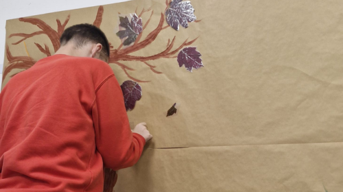 Ein Mann arbeitet an einem kreativen Poster. Er klebt Blätter an einen Baum. 