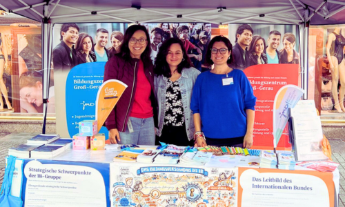 Unser Team am Informationsstand auf der Eröffnungsfeier der Interkulturellen Wochen. Man sieht einen Infostand mit vielen Materialien: Flyer und vieles mehr.