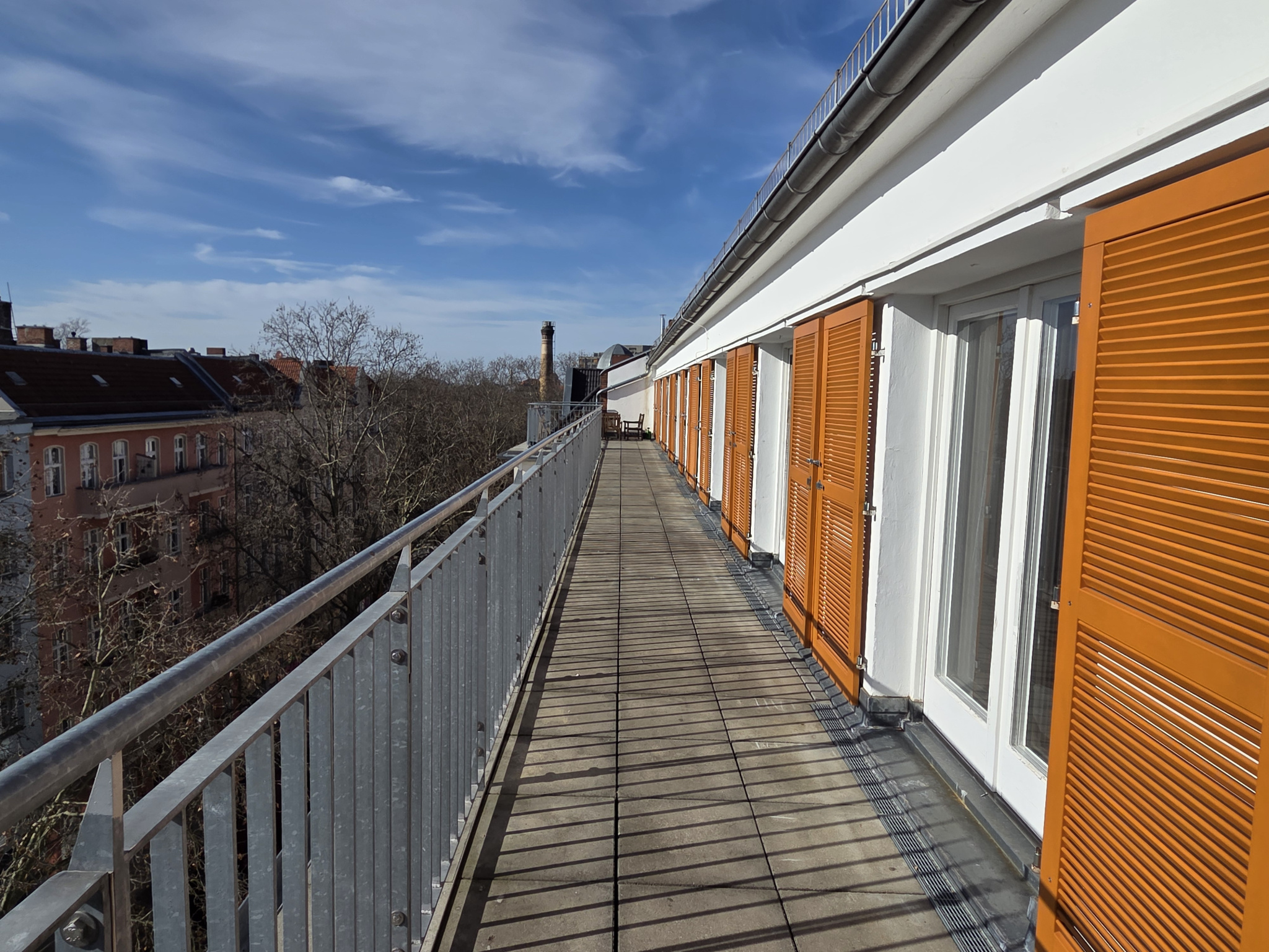 Eine Dachterrasse mit einem grauen Geländer auf die mehrere Türen führen.