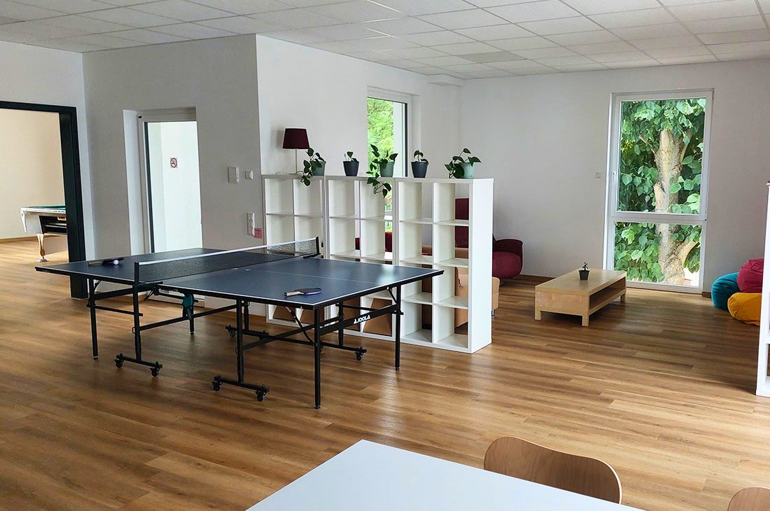 Ein großer, heller Raum mit einer Tischtennisplatte und einem weißen Kalax Regal, im Hintergrund ein Sofa und ein Kaffeetisch