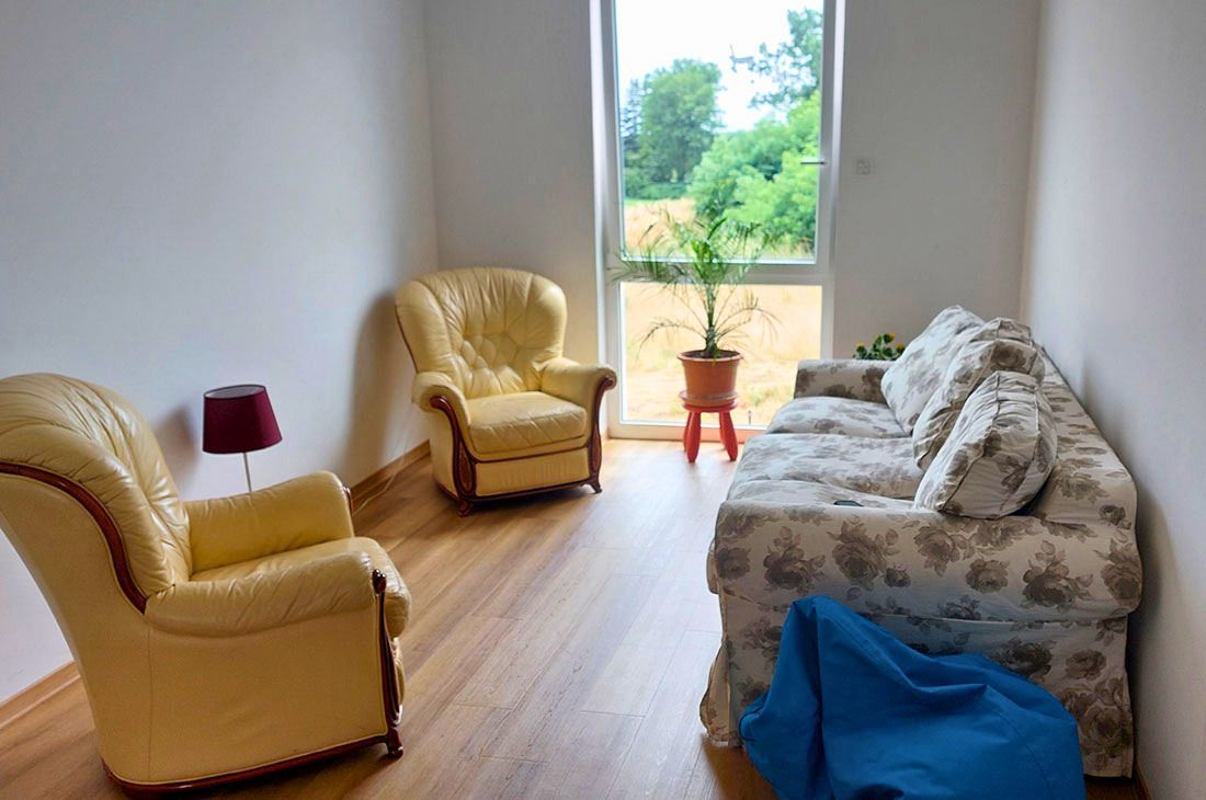 Ein kleiner Raum mit einem geblümten Sofa, zwei gelben Sesseln und einer Pflanze vor einem Fenster.