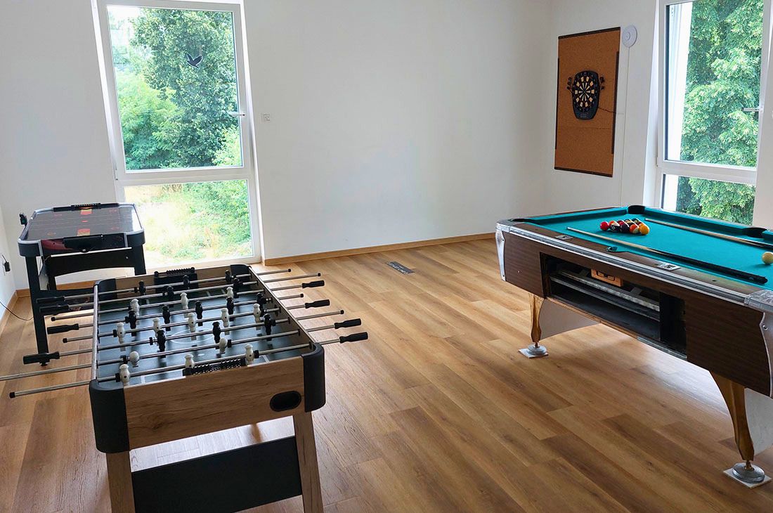 Ein großer heller Raum mit Billardtisch, ein Kickertisch, ein Air Hockey Tisch und einer Dart Scheibe an der Wand